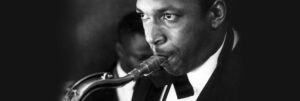 photo noir et blanc en gros plan de John Coltrane, en costume et noeud papillon, soufflant dans son saxophone. achetez le vinyle 